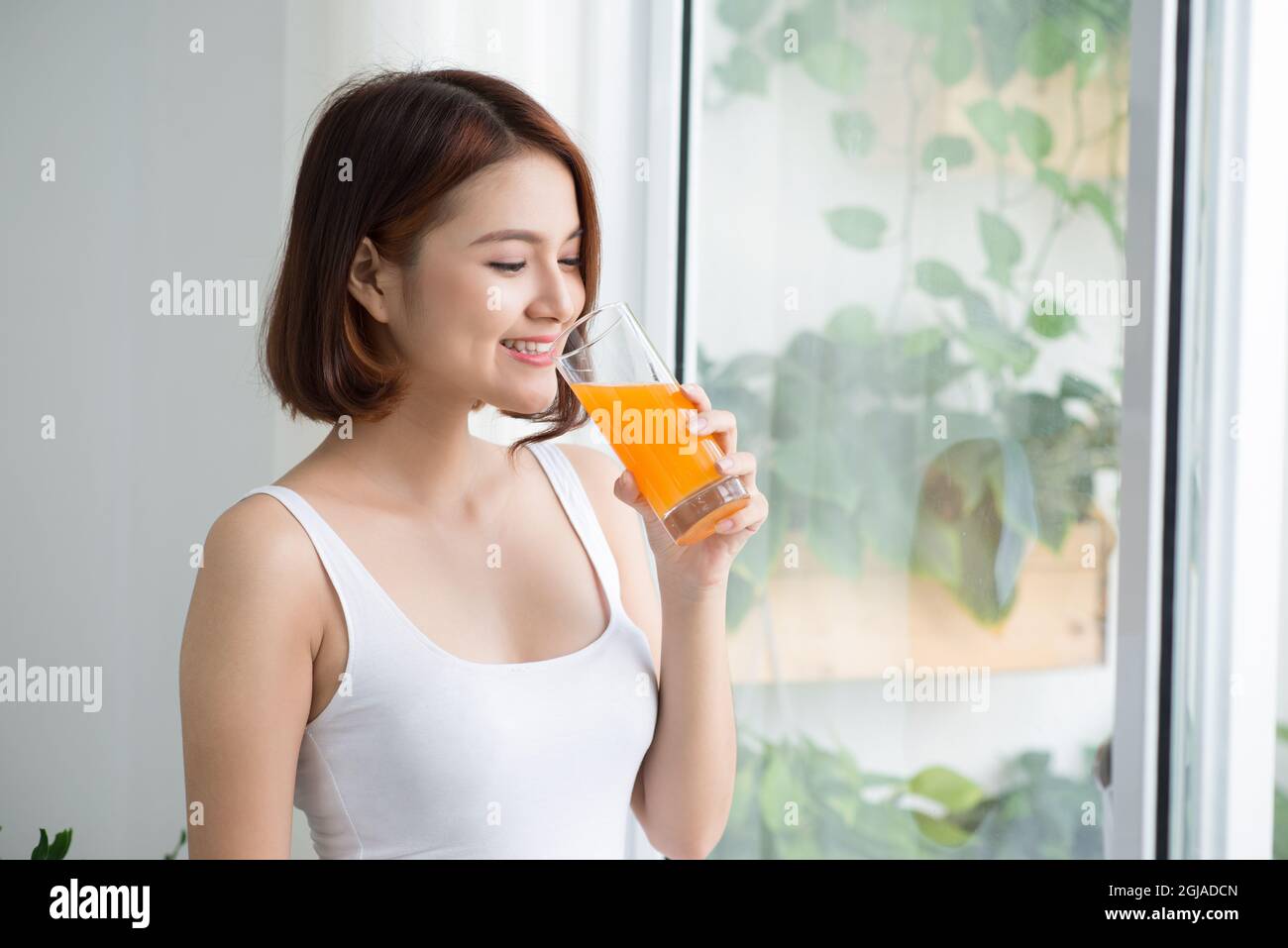 Ziemlich junge asiatische Frau in hellen Raum trinken Orangensaft Stockfoto
