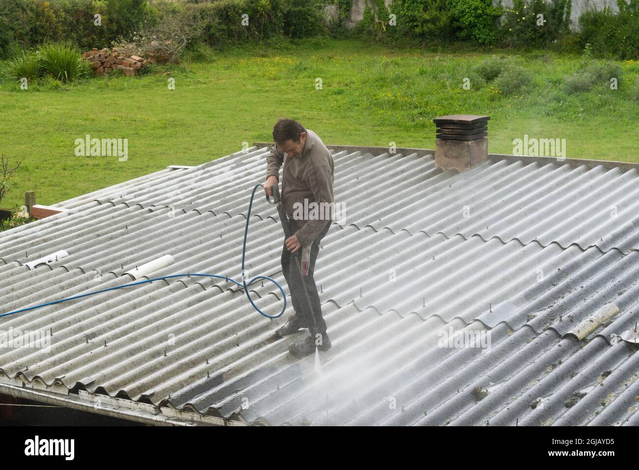 Mann, der ein Dach mit einer Druckwasserpistole reinigt Stockfoto