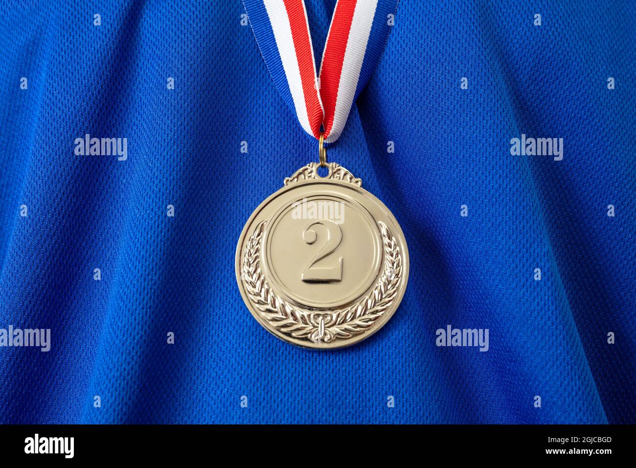Medaille in Silber. Siegerpreis hängt mit rot blauem Farbband auf der Brust des Sportlers. Trophäe im Sport für den zweiten Platz Champion auf blauem Hemd BA Stockfoto