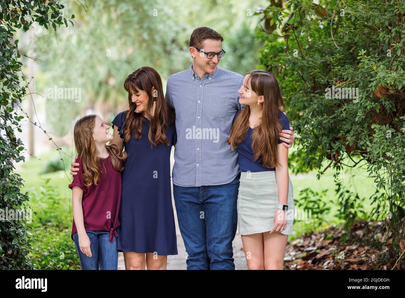 Eine Familie mit Mutter, Vater und zwei Töchtern, die im Sommer oder Herbst draußen auf dem Bürgersteig stehen Stockfoto