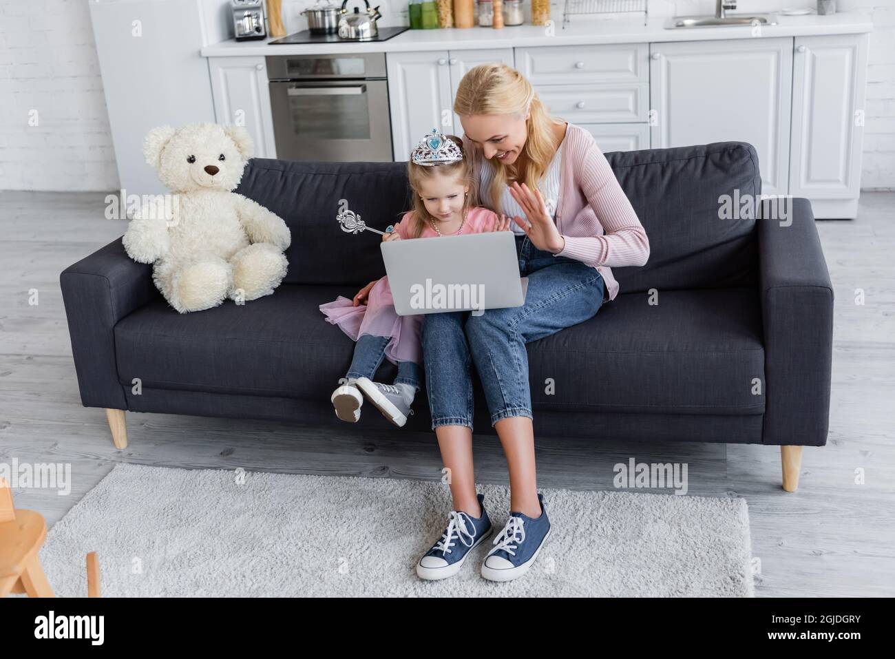 Glückliche Frau mit Tochter in Spielzeug Krone winkende Hände während Videoanruf zu Hause Stockfoto