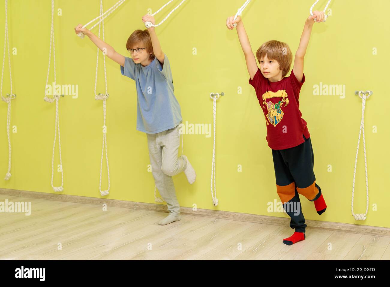 Zwei Jungen machen Übungen an einer gelben Wand mit Seilen. Jungen gehen mit einem Lehrer Sport. Stockfoto