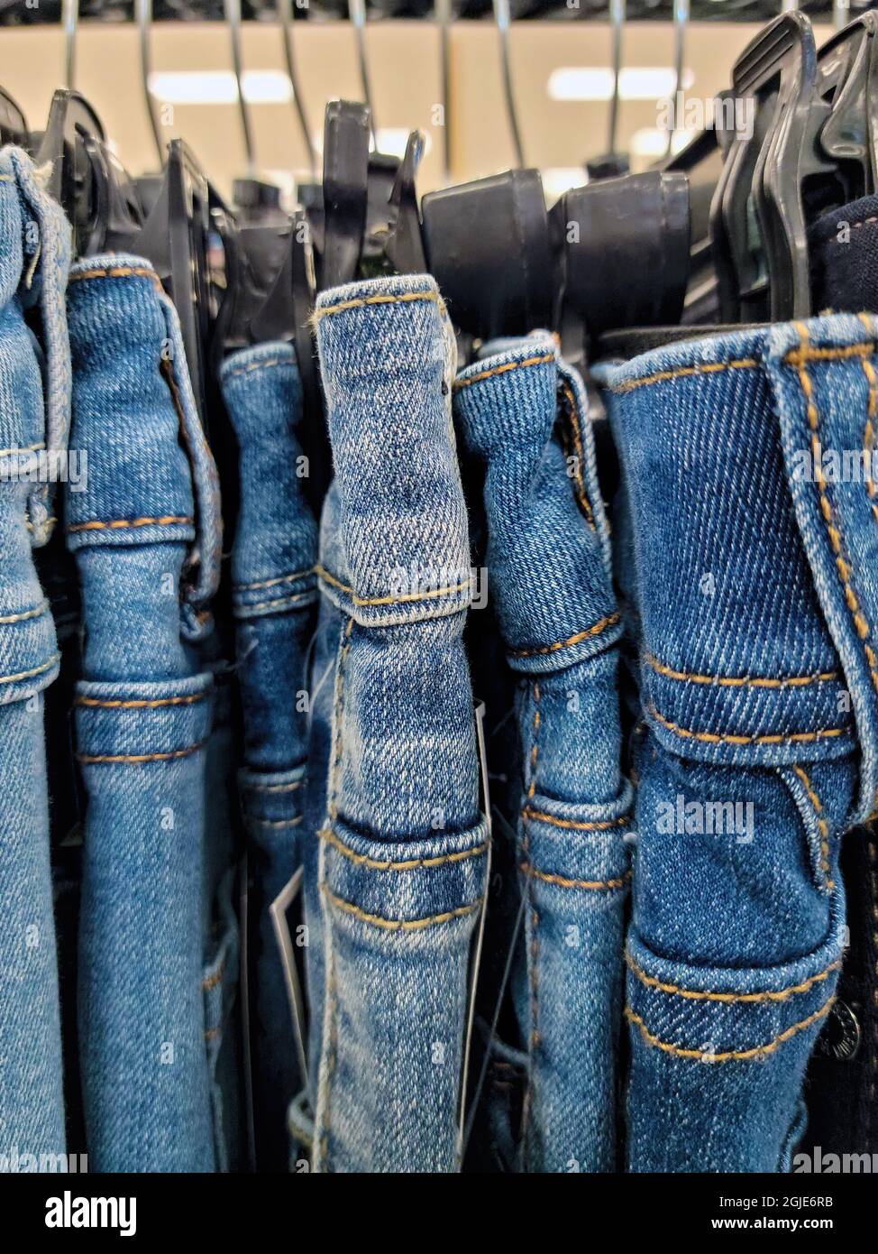 Nahaufnahme einer Reihe Jeans in Denim-Blau, die auf Kunststoffhangars im Geschäft hängen Stockfoto