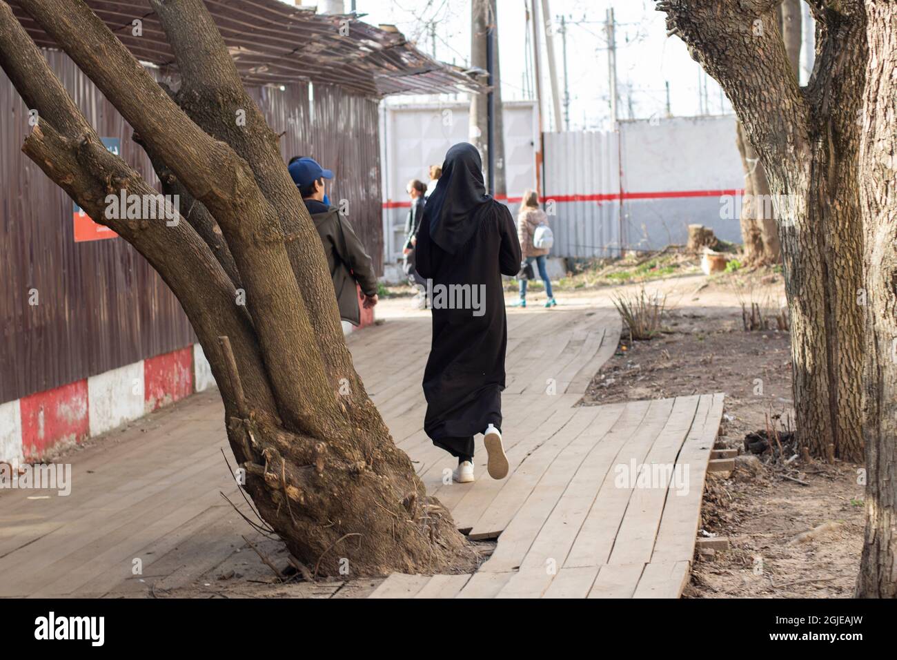 Eine Frau in einer schwarzen Burka geht die Straße entlang. Eine muslimische Frau geht durch die Stadt. Ein Stadtbewohner von hinten. Stockfoto