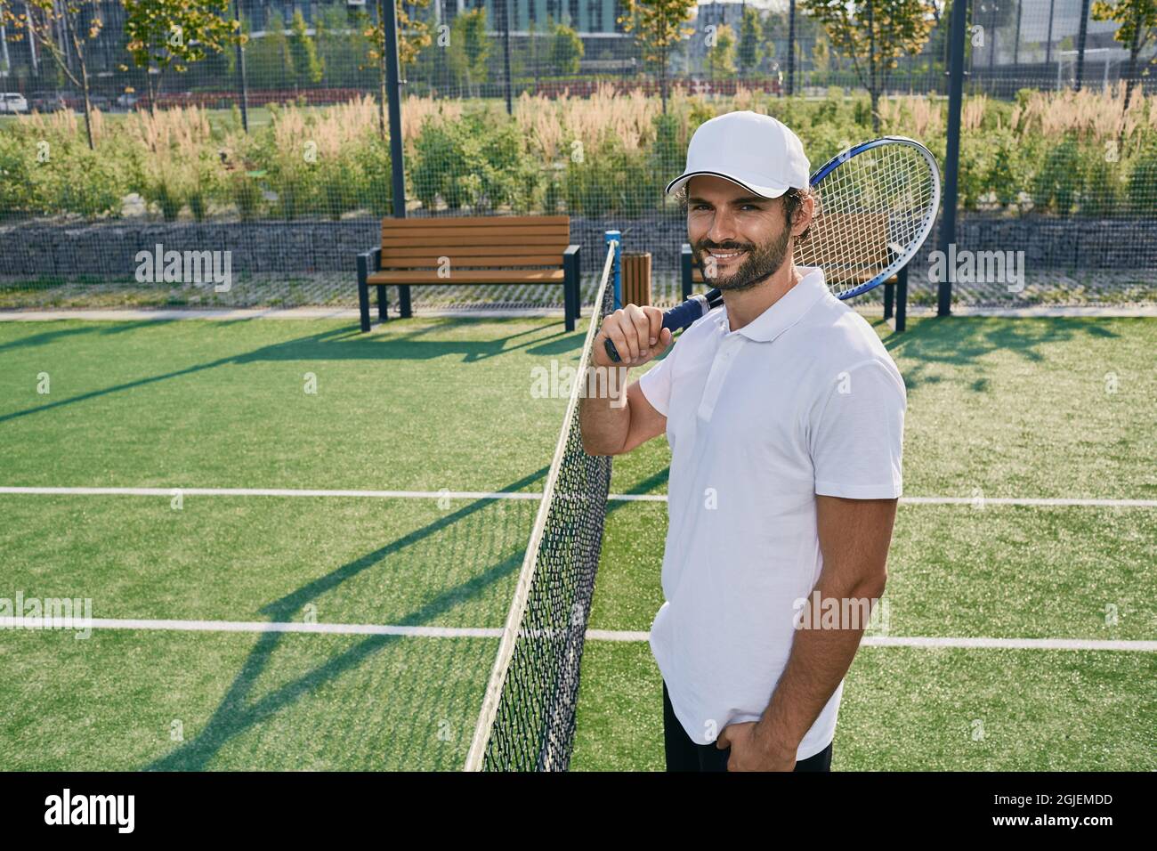 Professioneller Tennisspieler mit Schläger, der in der Nähe des Netzes auf dem Rasen-Tennisplatz posiert Stockfoto