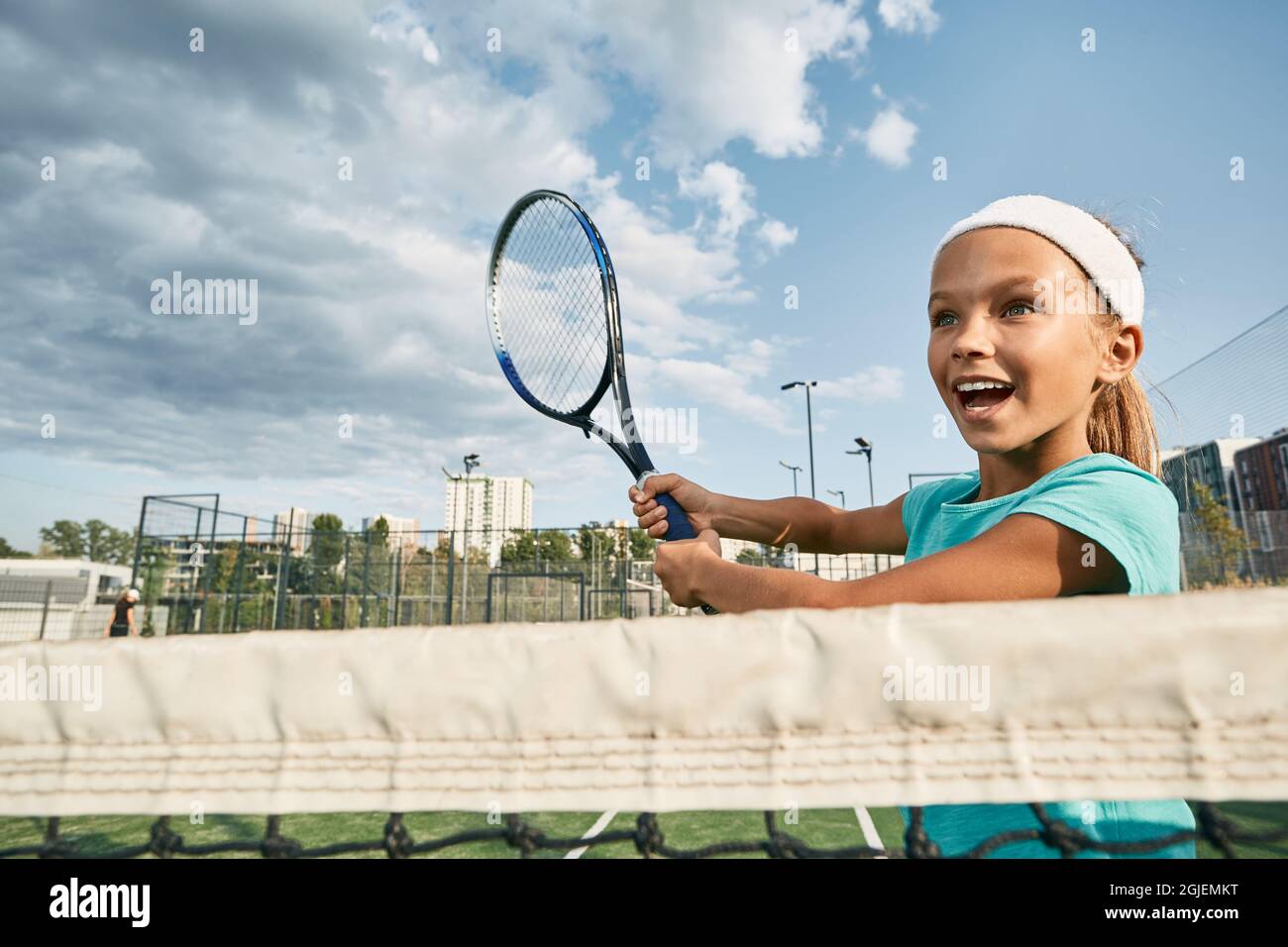 Schöne weibliche Kinder-Tennisspielerin, die in der Nähe des Netzes mit Vorhand spielt, während sie auf dem Stadtplatz im Freien Tennis spielt, mit Blick aus der Nähe des Netzes Stockfoto