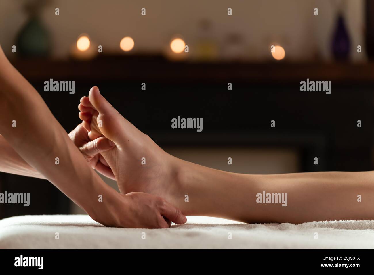 Masseur macht eine Fußmassage mit Kerzen auf dem Hintergrund Stockfoto