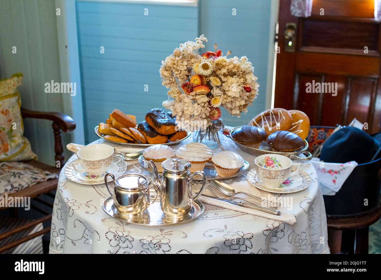 Eine formelle Einrichtung aus Desserts, silbernen Kaffee- und Teestäulen, porzellanbechern und Blumen auf einem Tisch für eine formelle Teeparty oder Feier. Stockfoto