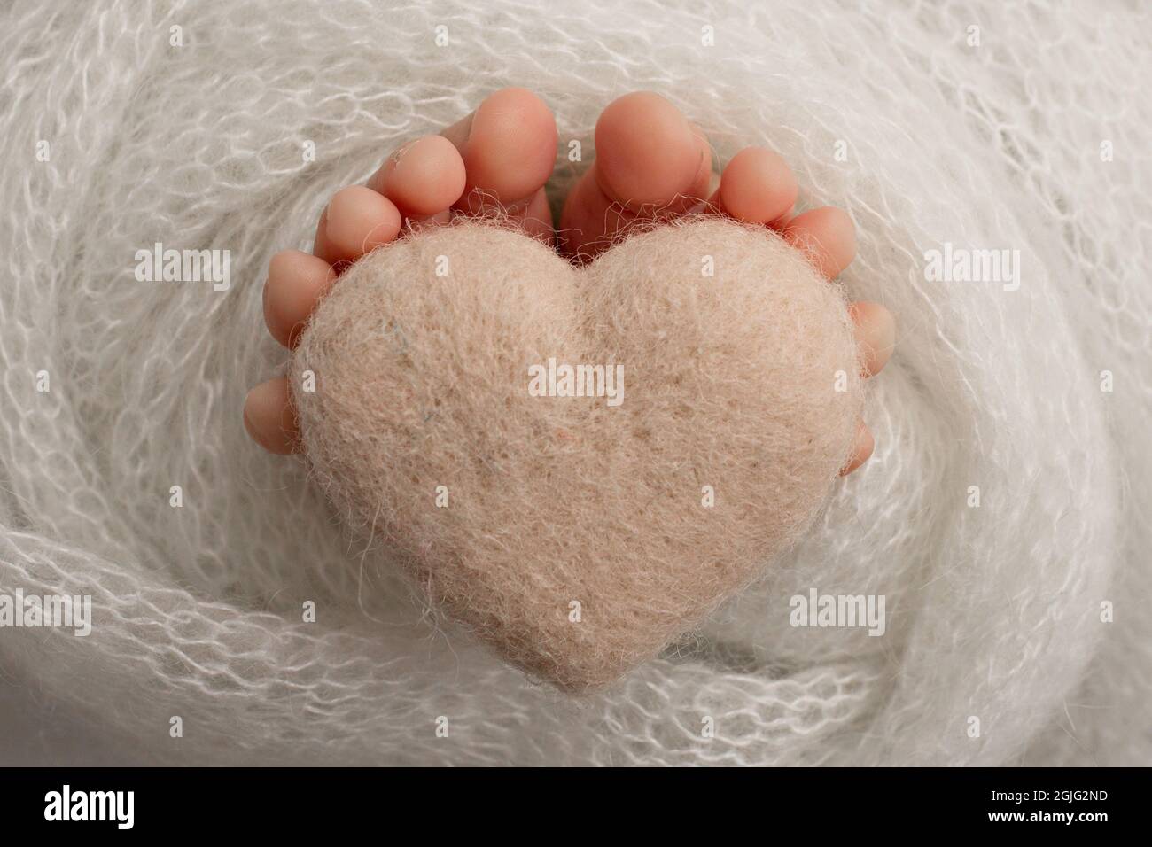 Beine eines Neugeborenen, weiche Strickdecke in weißer Farbe, gestricktes weißes Herz, Studiofotografie. Stockfoto