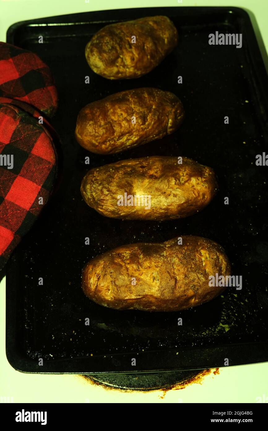 Gebackene Kartoffeln kühlen auf der Pfanne mit Ofenhandschuhen und stilisierten Retro-Farben Stockfoto