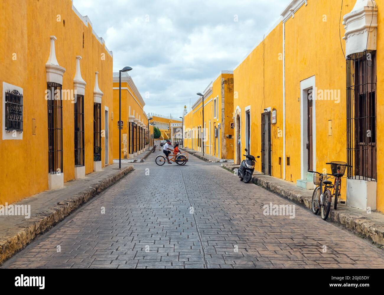 Mexikanischer Dreirad-Taxifahrer mit Beifahrer, der durch die Straßen der gelben Stadt Izamal im Kolonialstil fährt, Izamal, Mexiko. Stockfoto