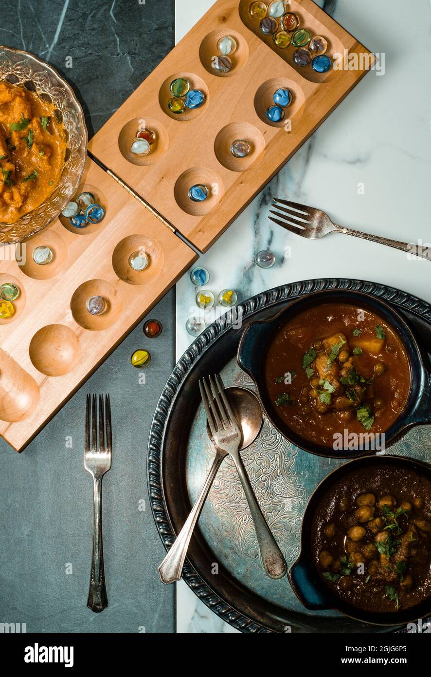 Spielen von Mancala Brettspiel beim Essen von indischem Essen einschließlich Huhn Tikka und pindi Chana Masala sowie Aloo Matar Stockfoto