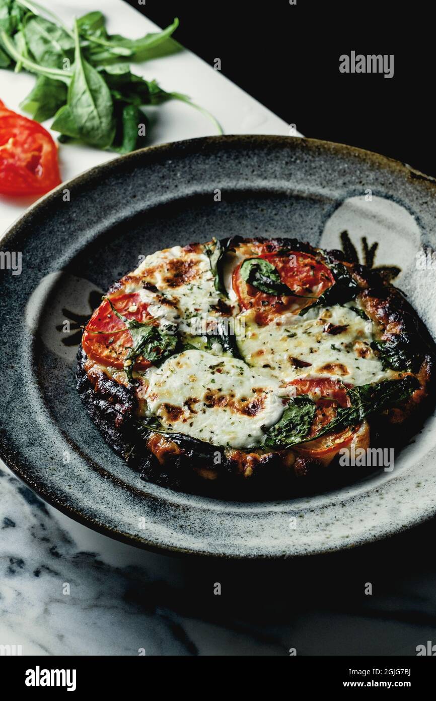 Mini-Pizza mit Tomatenscheiben und Spinat, geröstet im Backsteinofen Stockfoto