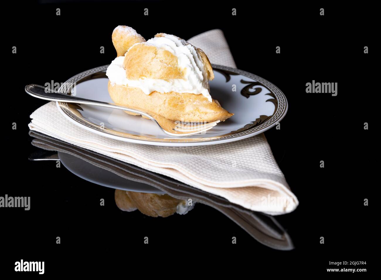 Cremepuff mit Schlagsahne auf einem weißen Teller mit beigefarbener Serviette und einer silbernen Gabel Stockfoto
