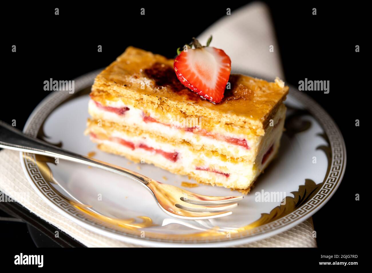 Erdbeer Napoleon auf einem weißen Teller mit beigefarbener Serviette und einer silbernen Gabel Stockfoto
