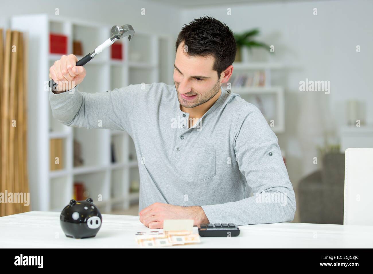mans Hand hält Hammer mit Sparschwein Stockfoto