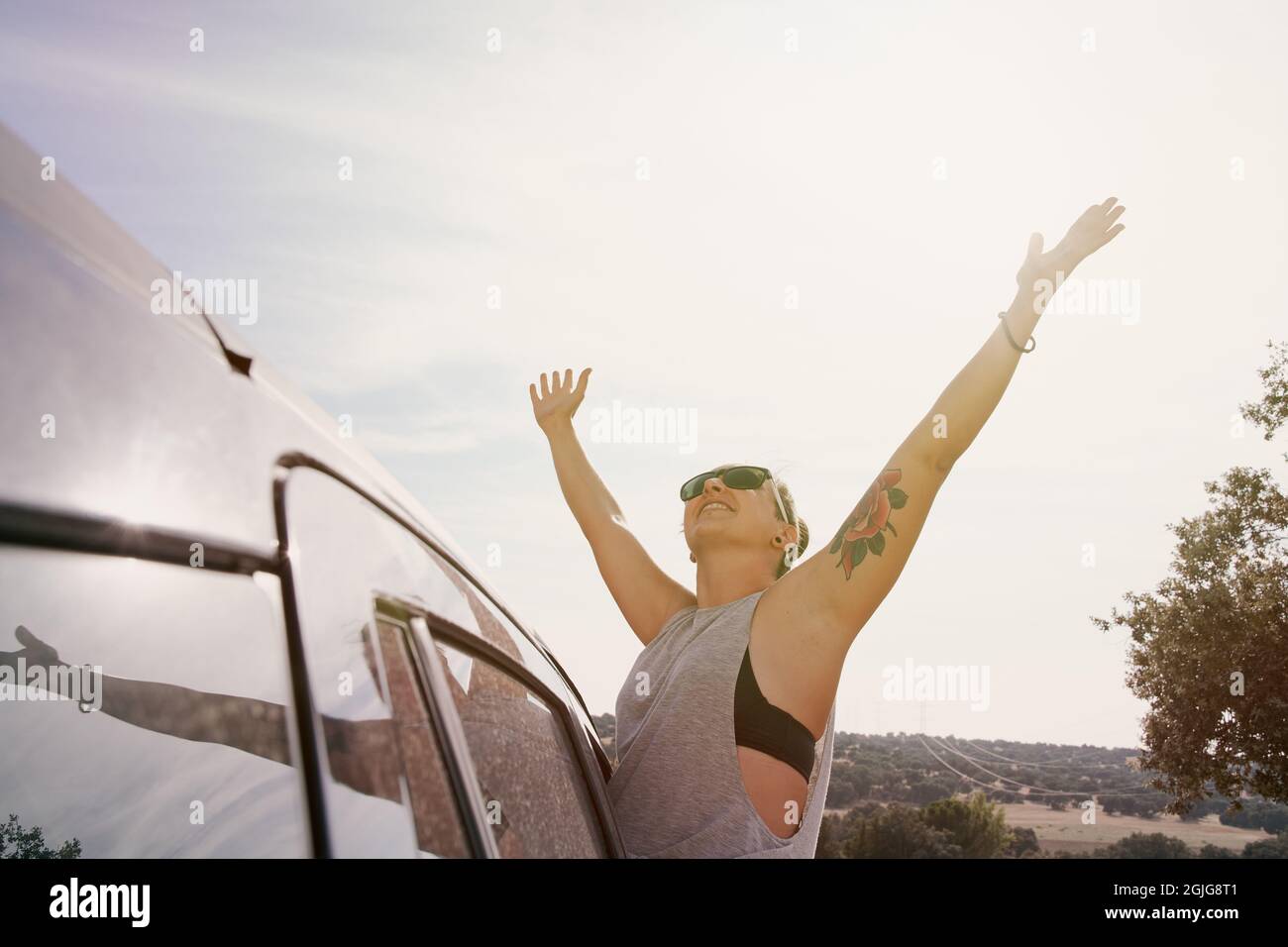 Frau, die aus dem Autofenster blickt und die Arme vor Glück angehoben hat. Konzept von Reisen, Lifestyle und Freizeitaktivitäten. Stockfoto