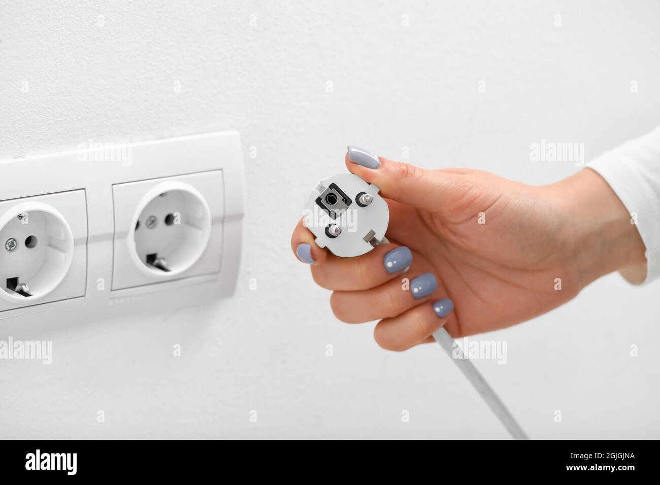 Eine Frau steckt den Stecker in die Steckdose im Zimmer Stockfoto
