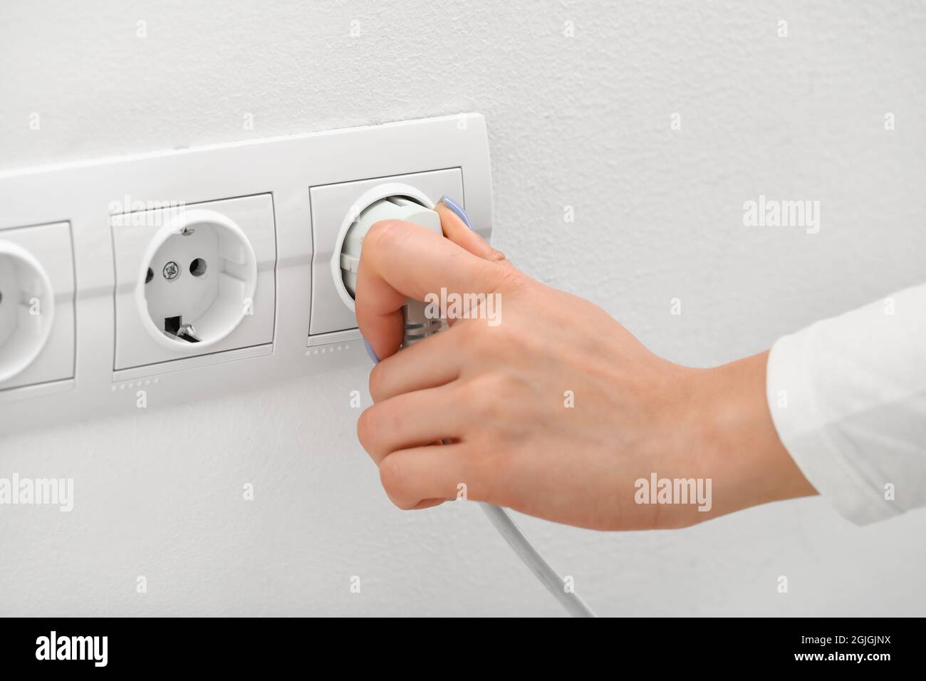Eine Frau steckt den Stecker in die Steckdose im Zimmer Stockfoto