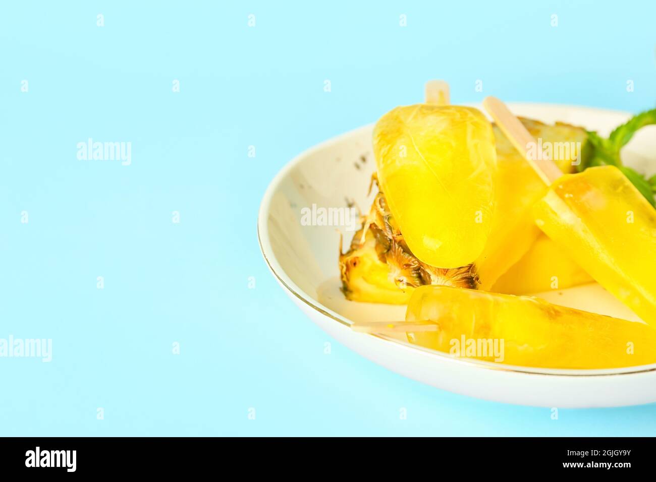 Teller mit leckeren Ananaspopsicles auf farbigem Hintergrund Stockfoto