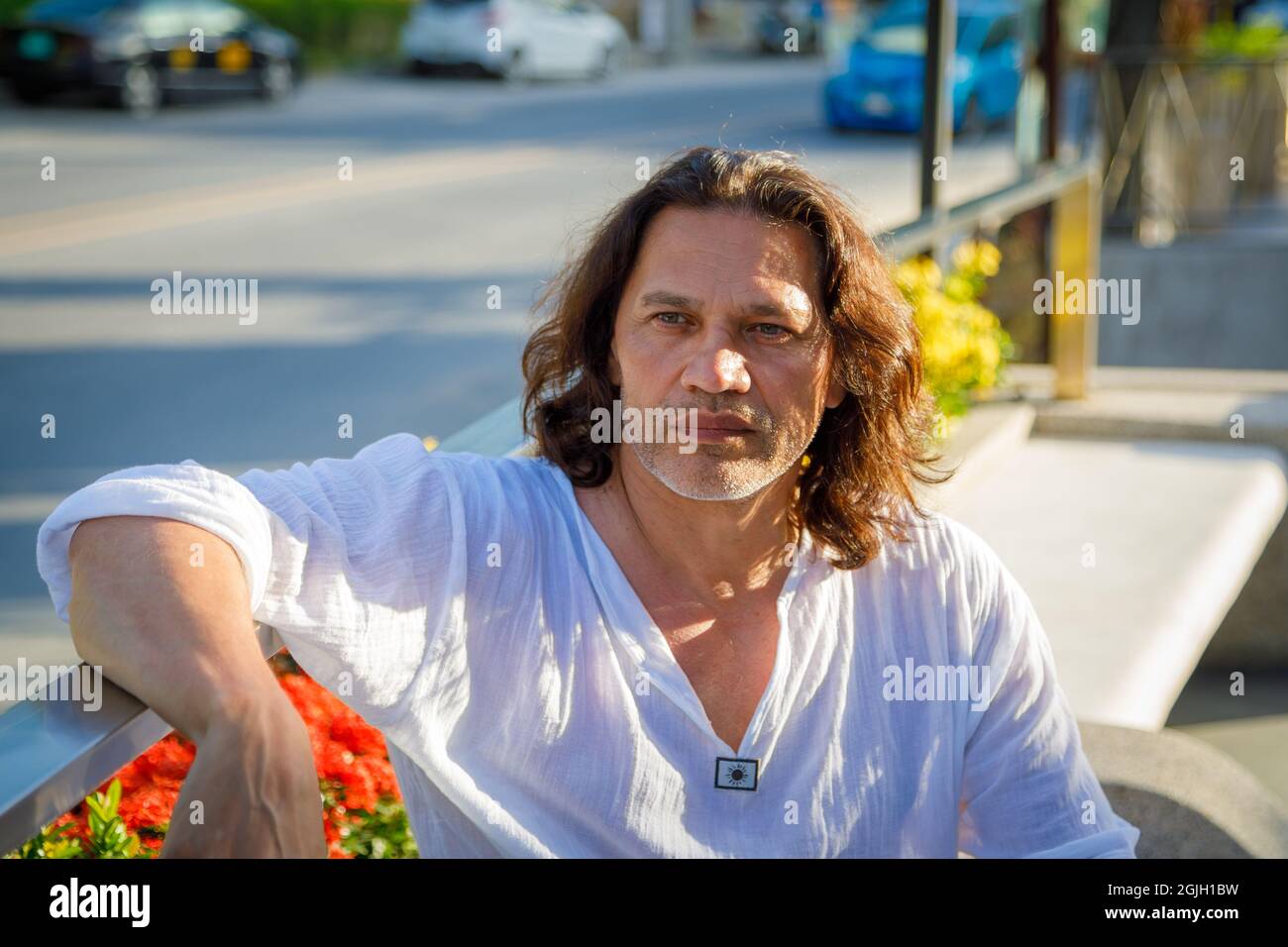 Ein erwachsener Mann mit langen Haaren und einem weißen Hemd schaut in die Ferne. Sommerferien. Stockfoto