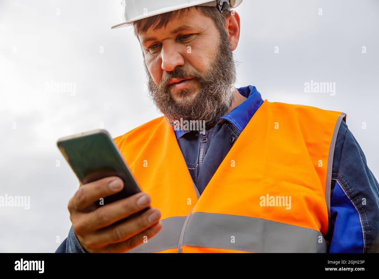 Ein Bauingenieur schaut auf ein Mobiltelefon. Ein bärtiger Mann sucht auf seinem Handy nach Informationen. Stockfoto