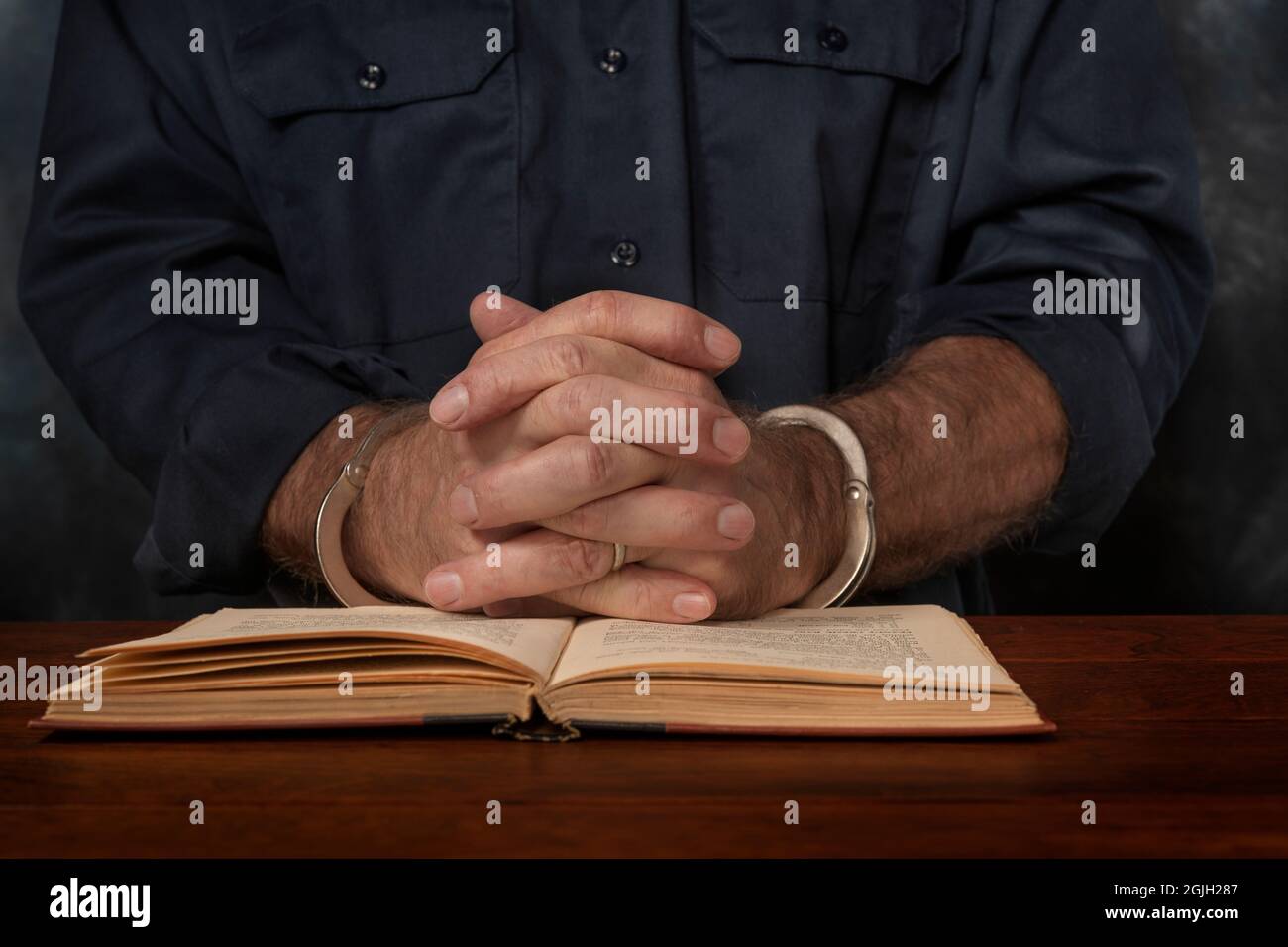 Ein verhaftete, mit Handschellen gefesselte Mann liest ein Buch über das Gesetz, in der Hoffnung, einen Weg zu finden, sich zu verteidigen. Stockfoto