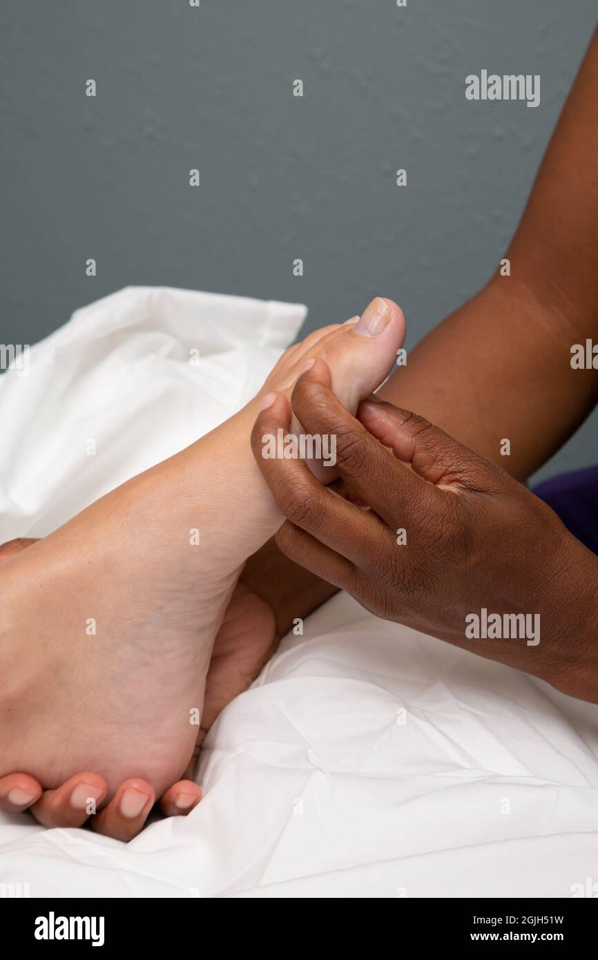 Schwarze weibliche Masseurin massiert den Fuß einer weißen Klientin Stockfoto