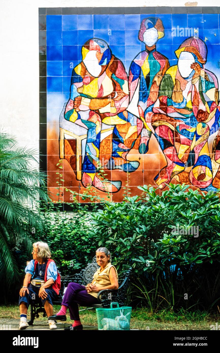 Damen entspannen in einem öffentlichen Park, mit Wandmalereien und Sträuchern, Havanna, Kuba Stockfoto
