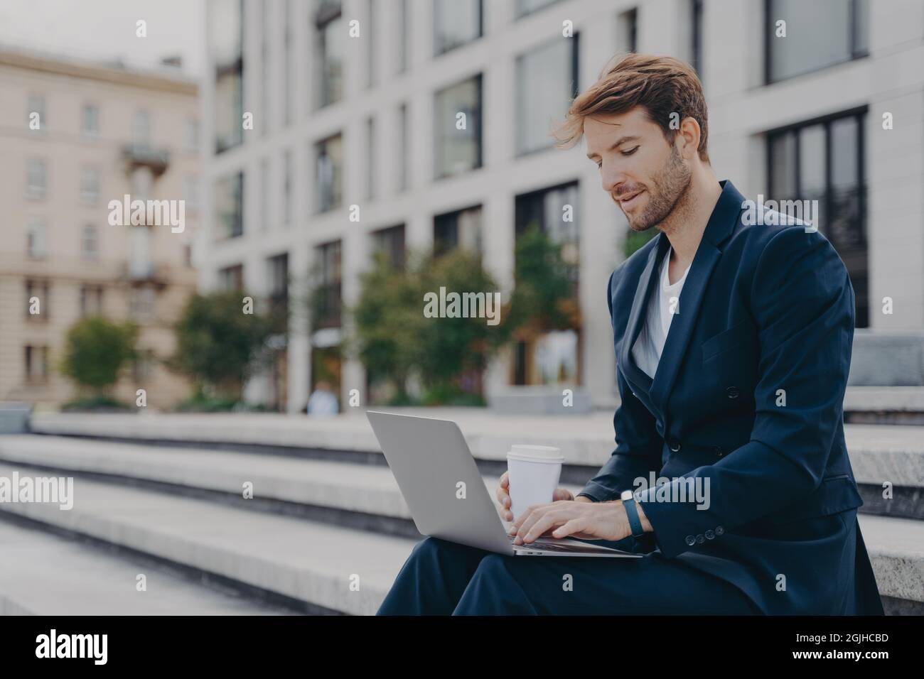 Geschäftsmann in formellen Anzug liest Nachrichten über Laptop-Computer arbeitet online Getränke zum Mitnehmen Kaffee Stockfoto