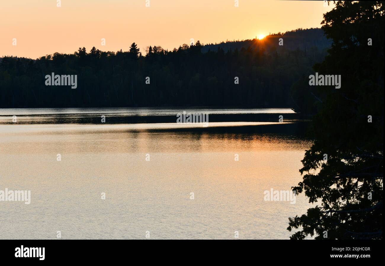 An einem warmen Sommertag geht die Sonne hinter den bewaldeten Hügeln am Bass Lake in der Nähe von Thunder Bay, Ontario, Kanada, unter. Stockfoto