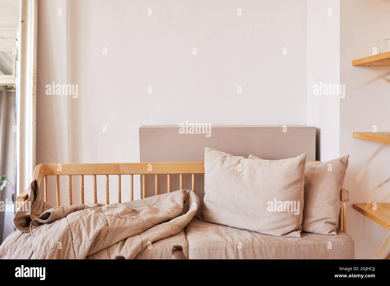 Fragment der häuslichen Einrichtung in natürlichen Pastelltönen mit Holzcouch mit weichen beigen Kissen und Deckelbezug an der weißen Wand Stockfoto