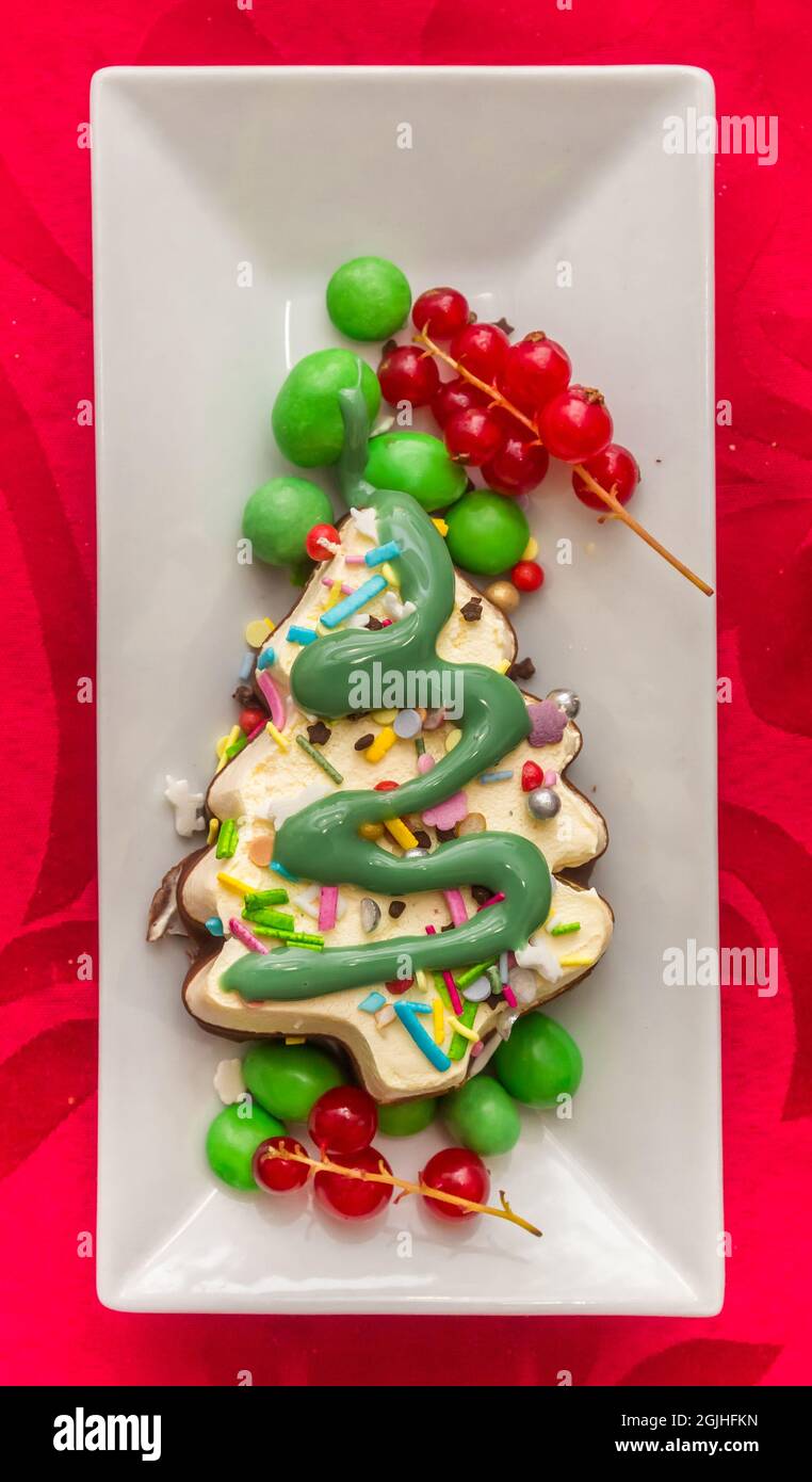 Eis in Form eines Weihnachtsbaums und mit Süßigkeiten und Früchten auf einem roten Tischtuch verziert Stockfoto