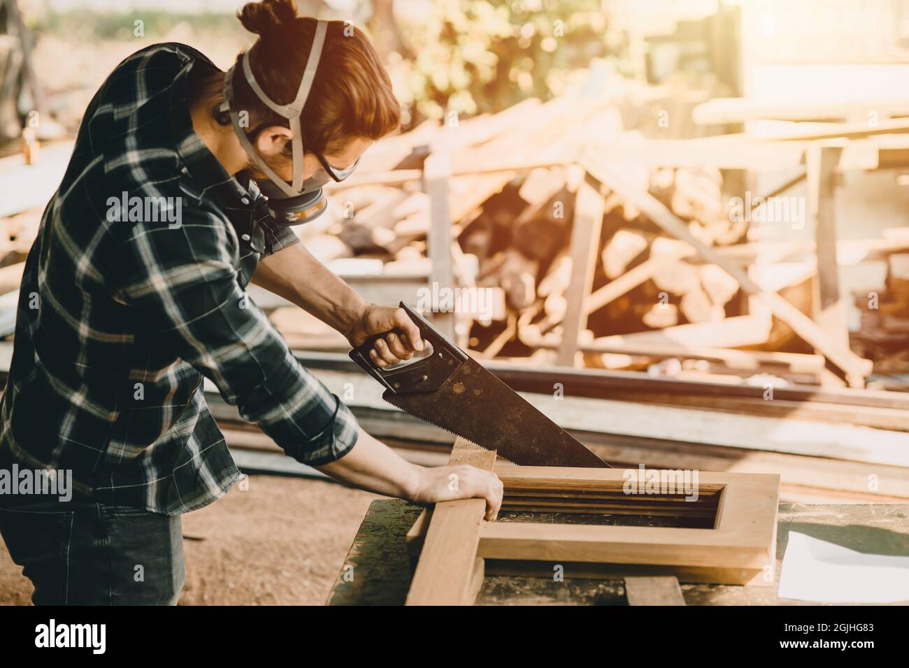 Männlicher Arbeiter, der Holz sägt, um Möbel in der Werkstatt mit Sicherheitsluftmaske der Industrie zu machen. Stockfoto