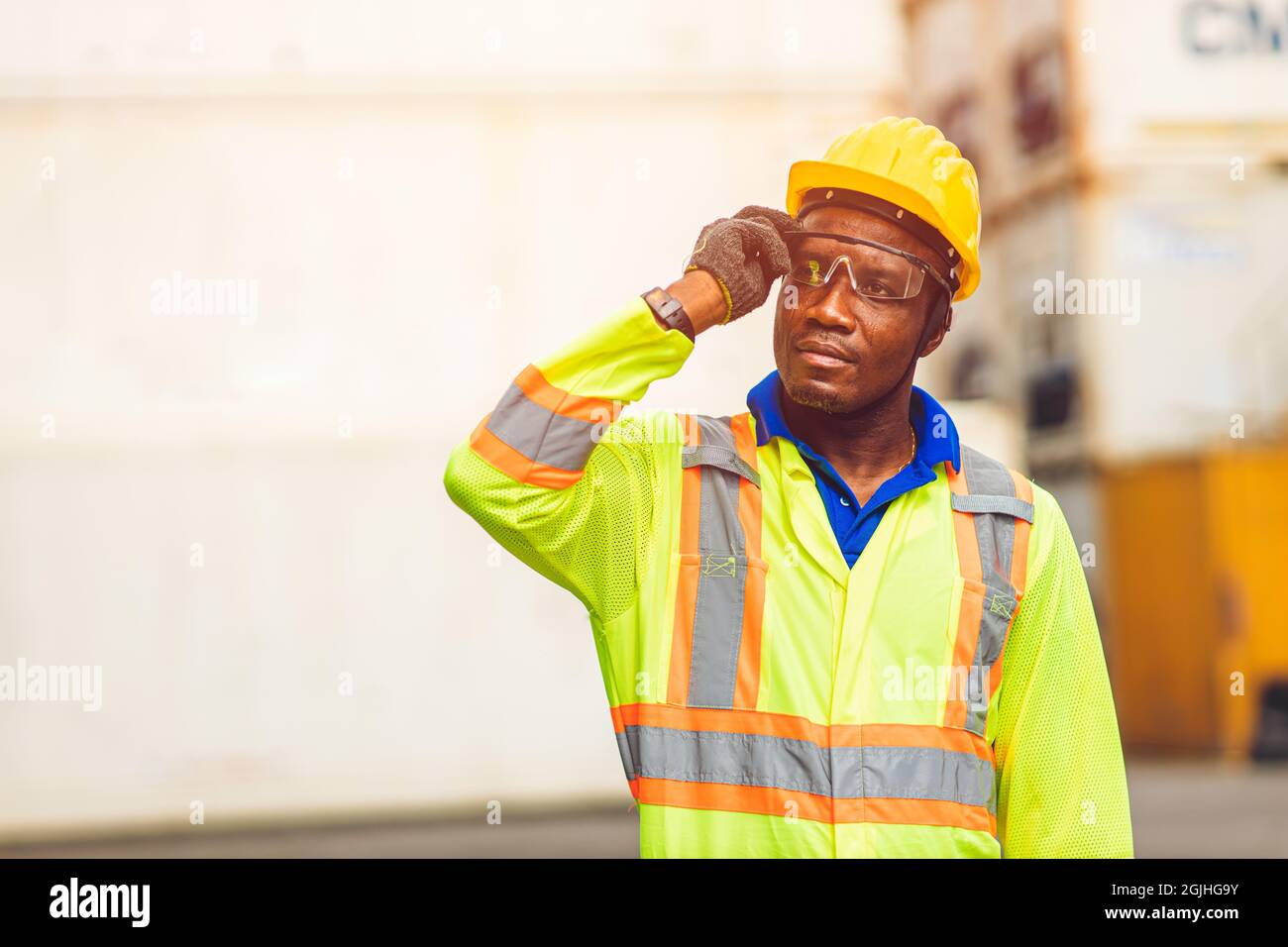 Schwarzer afrikanischer glücklicher Arbeiter, der in der Logistikschifffahrt arbeitet und selbstbewusst intelligente Container in der Hafenfrachtschifffahrtindustrie steht. Stockfoto