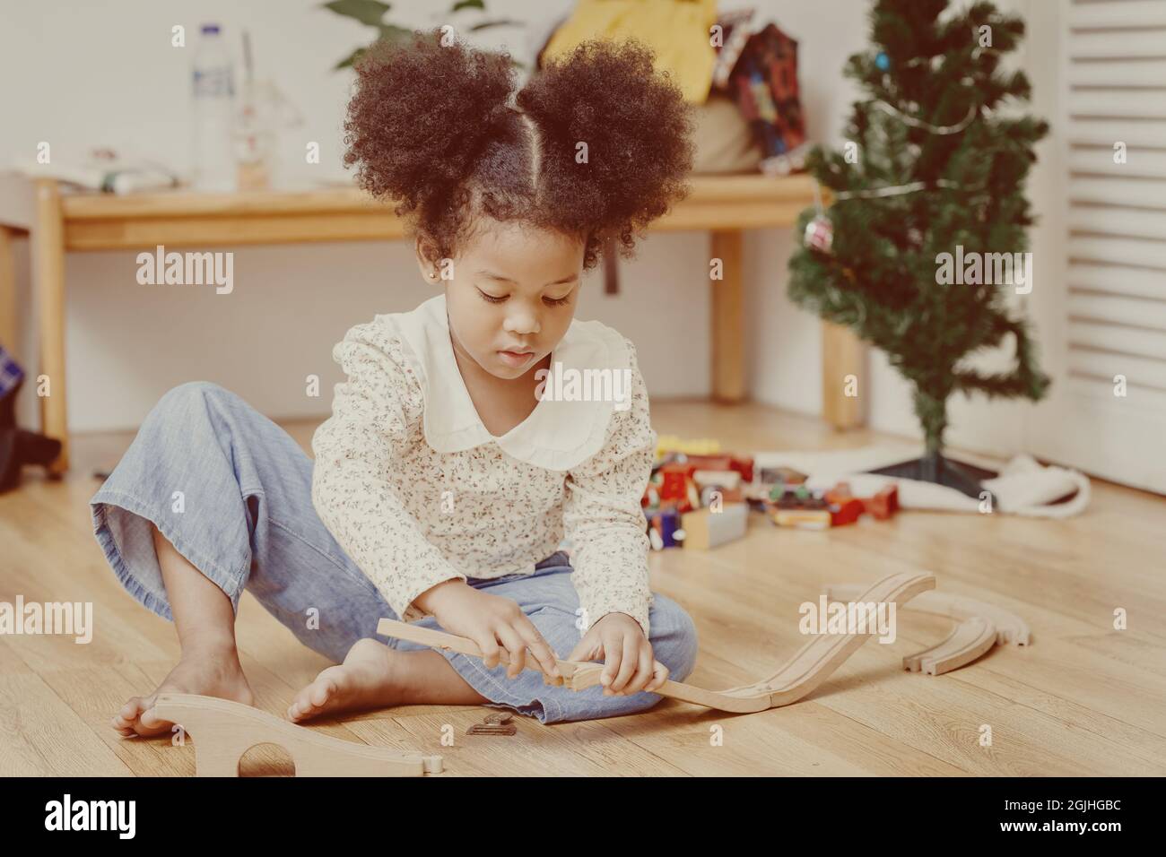 Schwarzes kleines Mädchen Kind spielt Holzspielzeug zu Hause allein vintage Farbton. Stockfoto
