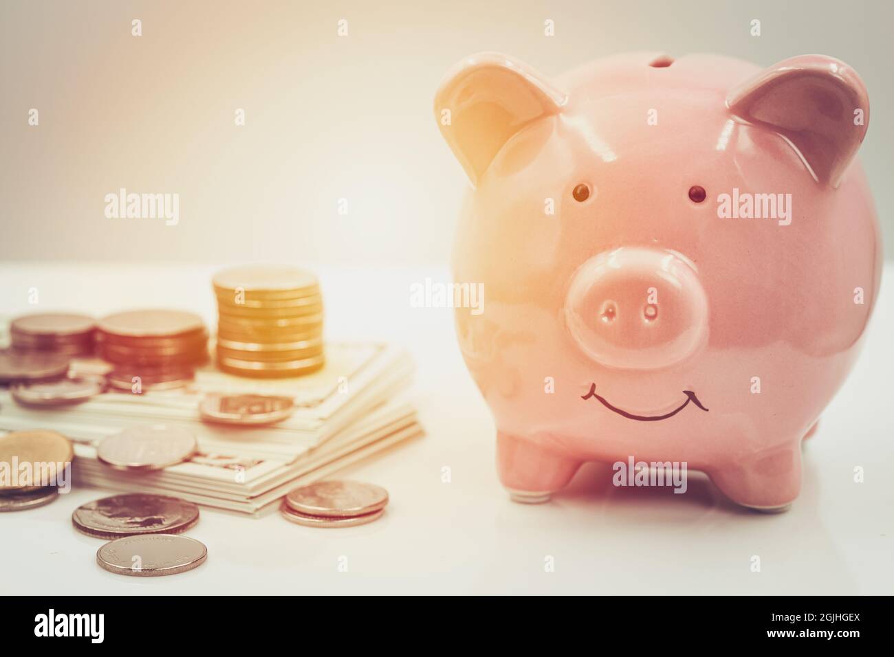 Fröhliches, lächelndes Sparschwein mit einem Haufen Münzgeld für das persönliche Einkommen, das Geld spart und ein finanzielles Konzept hat. Stockfoto