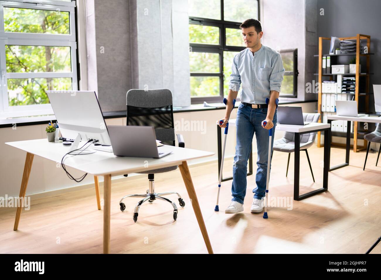 Arbeiter Mit Krücken Am Arbeitsplatz Oder Im Büro. Leistungen Für Die Rehabilitation Bei Handicap Stockfoto