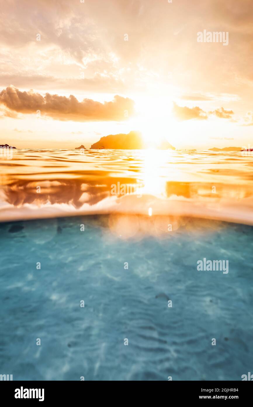 Split Shot, über unter der Wasseroberfläche. Unschärfe-Wellen im Vordergrund mit Tavolara Island an der Oberfläche während eines dramatischen Sonnenaufgangs. Stockfoto