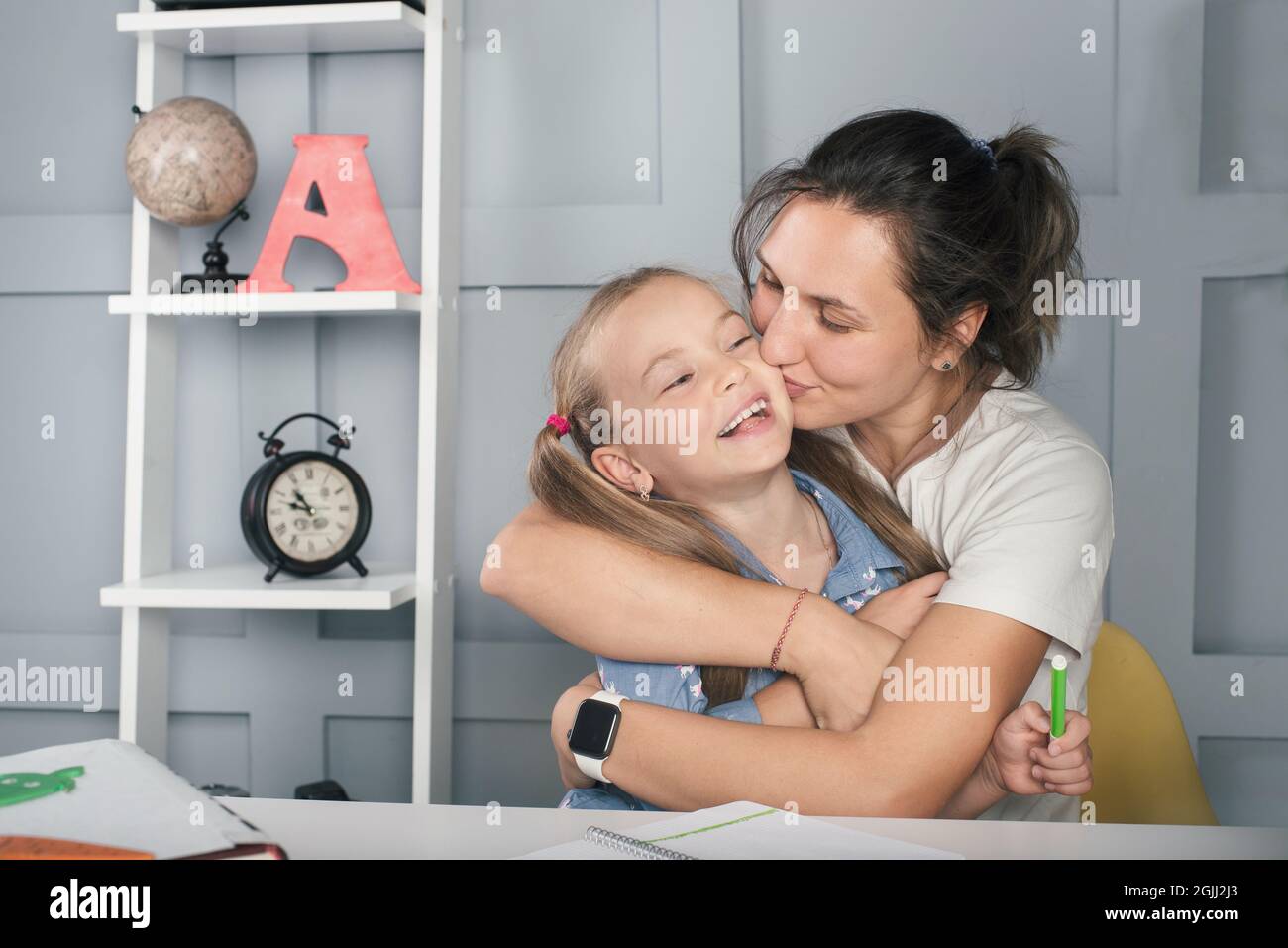 Positive Schulmädchen mit Mutter zu Hause lernen, umarmen und lachen. Familienbildung Stockfoto