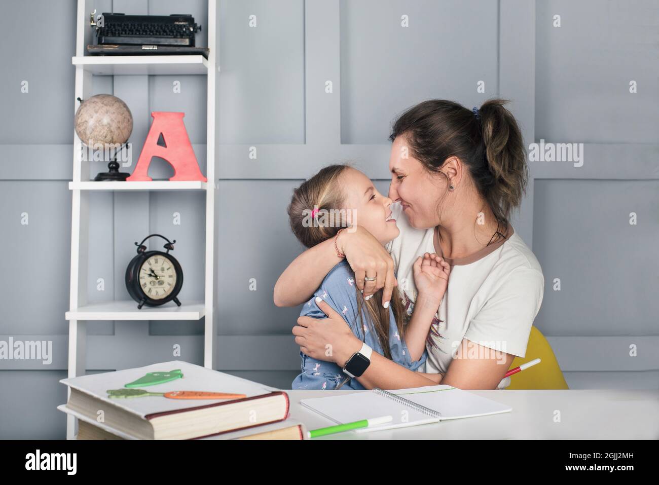 Positive Schulmädchen mit Mutter zu Hause lernen, umarmen und lachen. Familienbildung Stockfoto