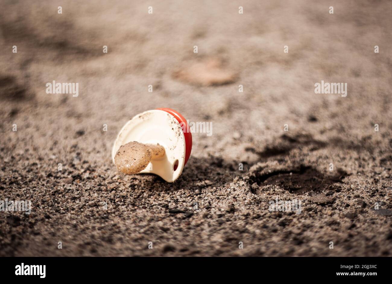 Schmutziger Babyschnuller auf dem Boden isoliert | Nahaufnahme des Babyschnupfes auf dem Boden liegend Baby-Schnuller mit Sand und Schmutz auf dem Boden bedeckt Stockfoto