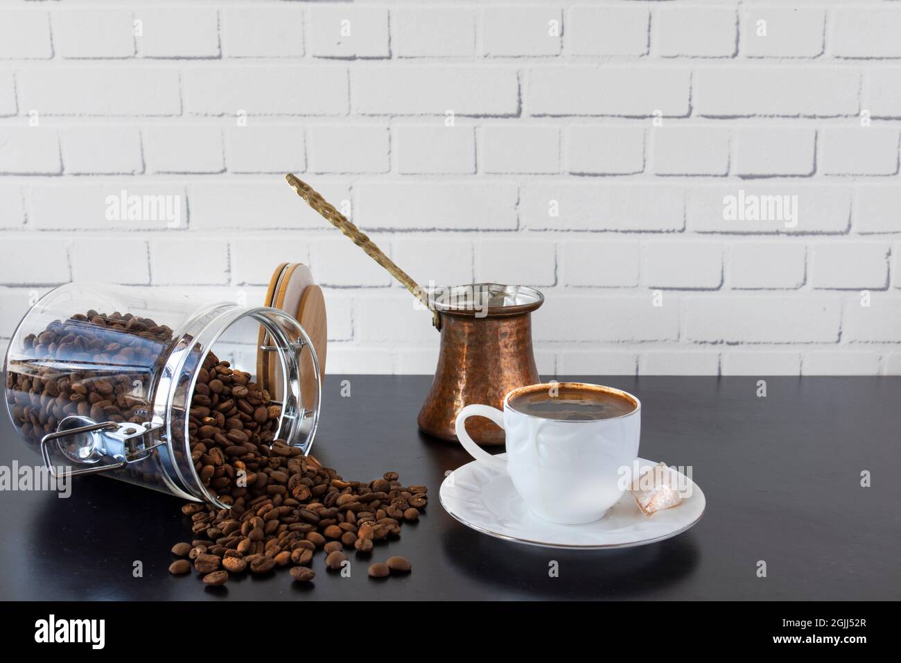 Vor einer weißen Backsteinmauer, auf schwarzem Hintergrund, eine Tasse türkischer Kaffee, türkischer Genuss, Kanne und ein Glas Bohnen. Selektiver Fokus. Stockfoto