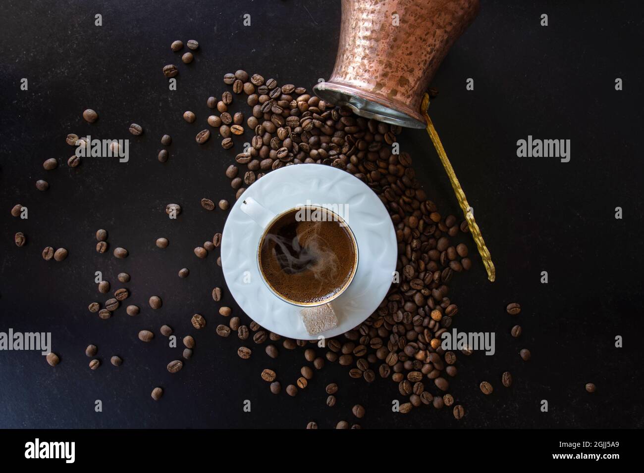 Türkischer Kaffee auf einer Tasse Rauch auf schwarzem Hintergrund. Verstreute Bohnen und ein umgedrehter Topf. Stockfoto
