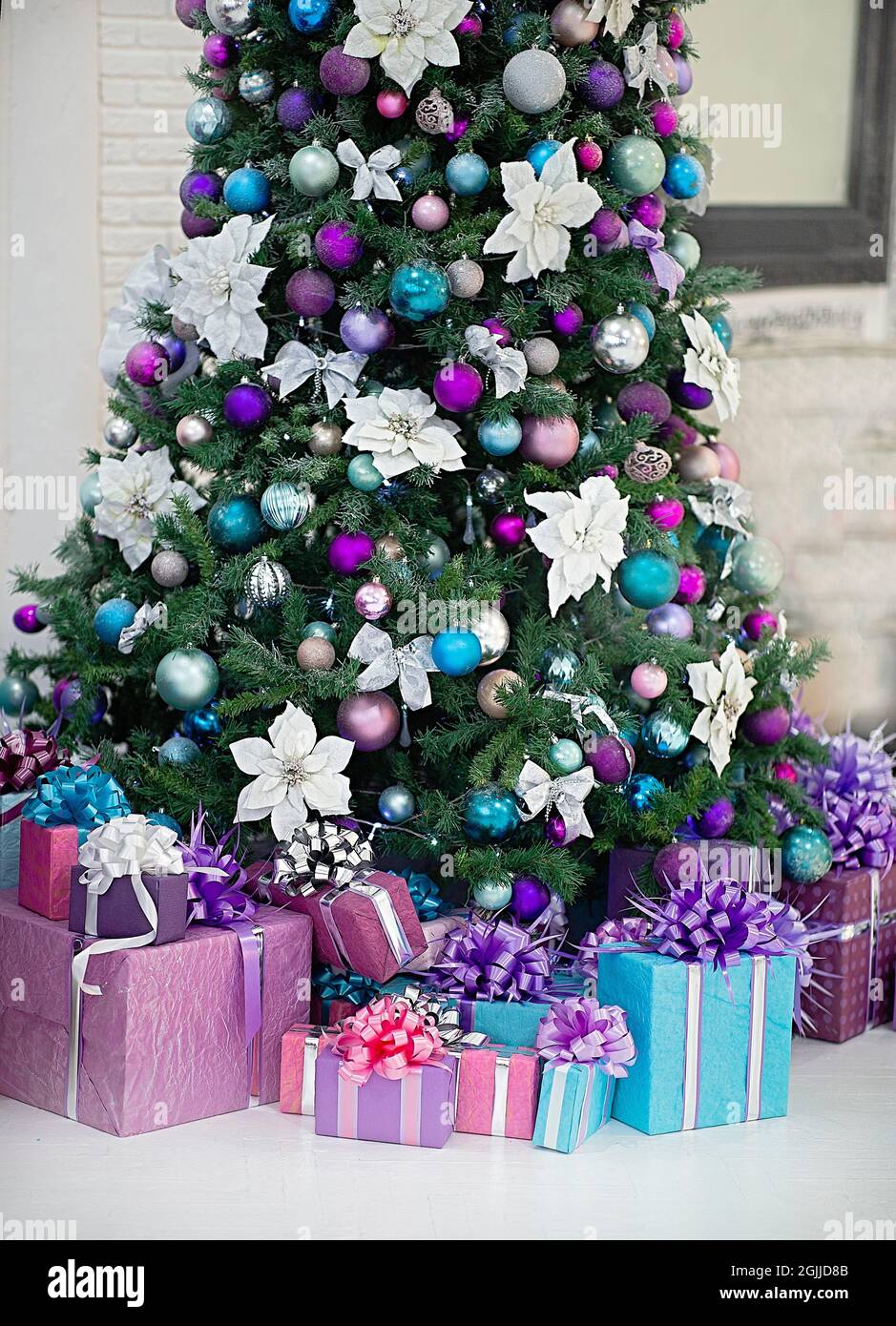 Wunderschön dekorierter Weihnachtsbaum. Darunter sind Geschenke. Die Hauptfarben der Spielzeuge: Weiß, lila, blau. Stockfoto