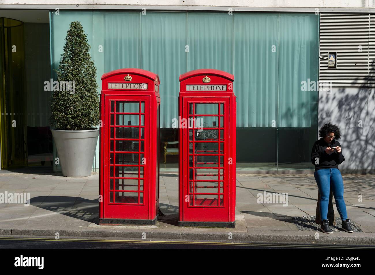 Frau, die ein Mobiltelefon benutzt, während sie an Telefonzellen sitzt, Saint Martin's Lane, London, Großbritannien. 18 April 2015 Stockfoto