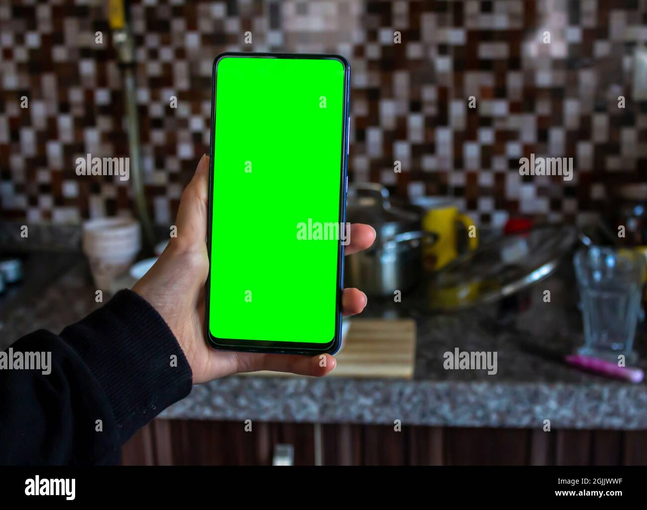Frau Hand hält grünen Bildschirm Handy in der Küche. Verschwommenes ungewaschene Geschirr im Hintergrund. Mockup-Bild, Kopierbereich. Stockfoto