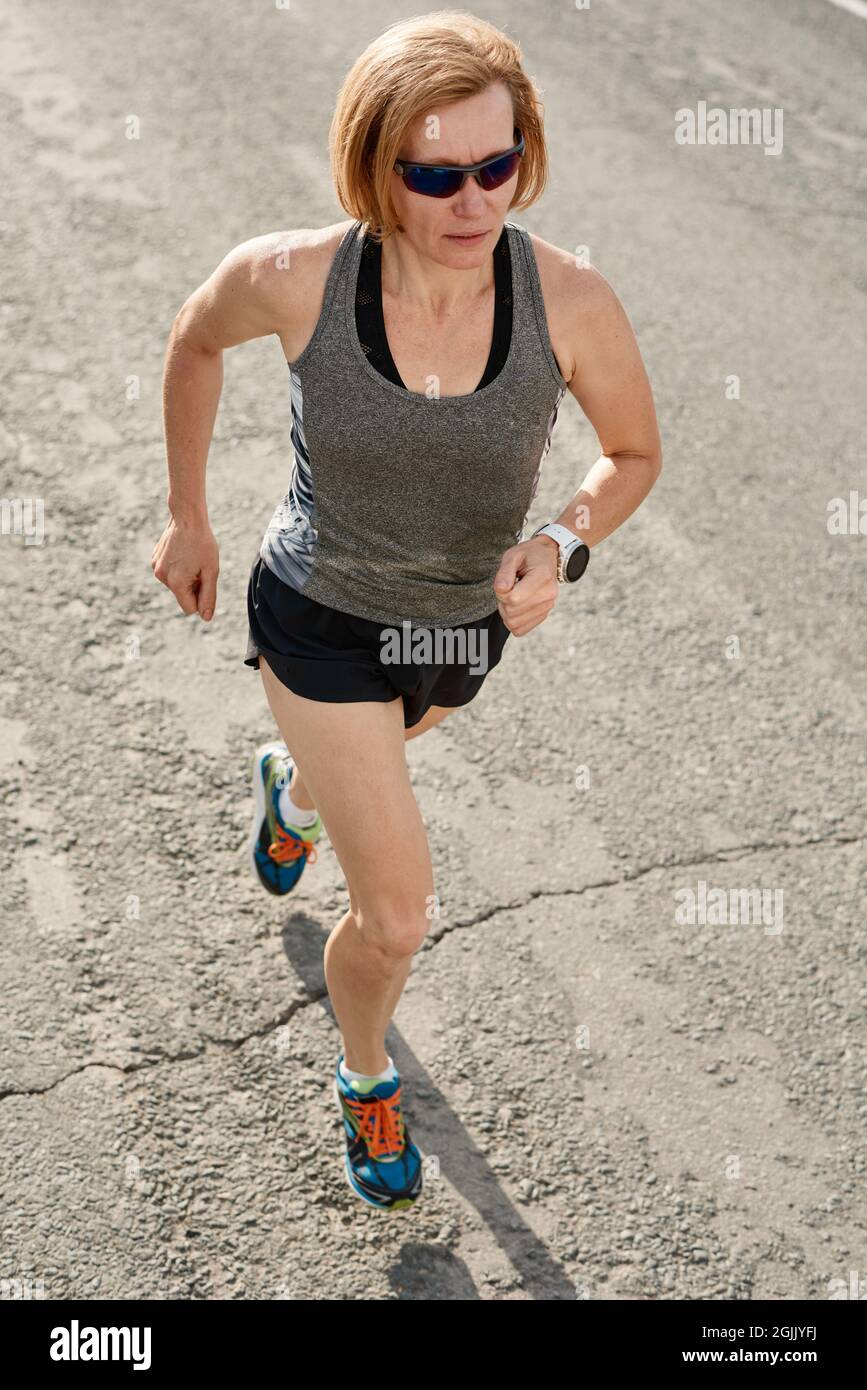 Reife Frau in Sonnenbrillen Läufer laufen auf Landstraße am Morgen Stockfoto