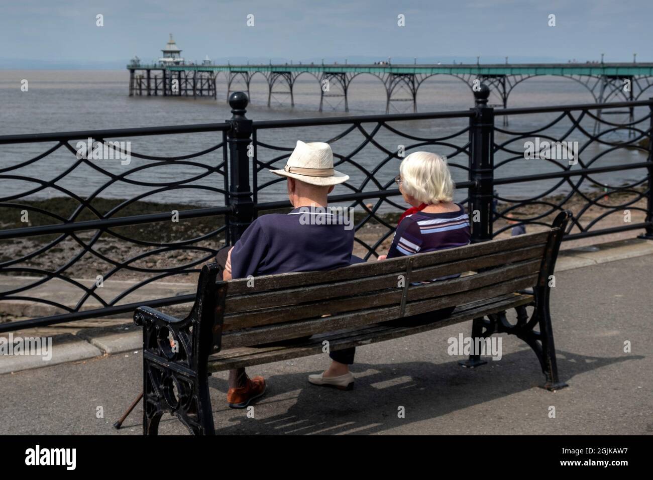 Ein älteres Paar, das auf einer Bank mit Blick auf den Clevedon Pier sitzt Stockfoto