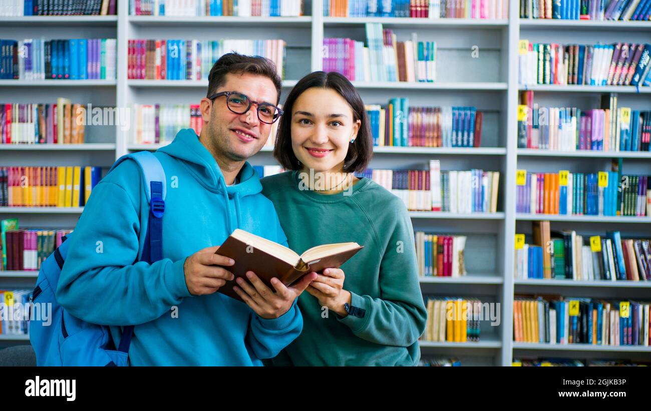 Eine junge, tausendjährige Studentin mit Brille und eine junge, attraktive Studentin lesen ein Buch und bereiten sich auf eine Prüfung vor, während sie in der Öffentlichkeit steht Stockfoto